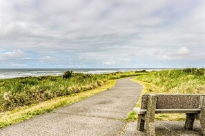 Ein gepflasterter Weg führt zu einer Bank mit Blick auf eine Küstenlandschaft, Gras und das Meer.