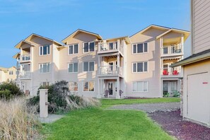 Kerrostalo, jossa on useita kerroksia, parvekkeita, pääsisäänkäynti ja pieni etupiha.