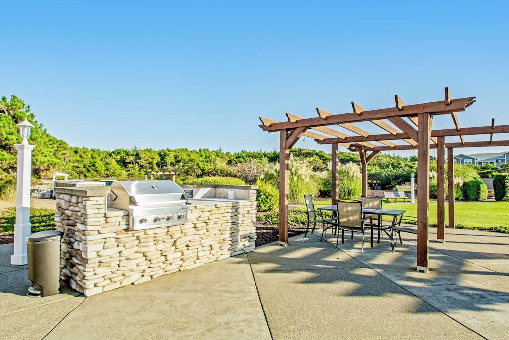 Un patio al aire libre con una estación de barbacoa de piedra, un pérgola de madera y zona de estar.