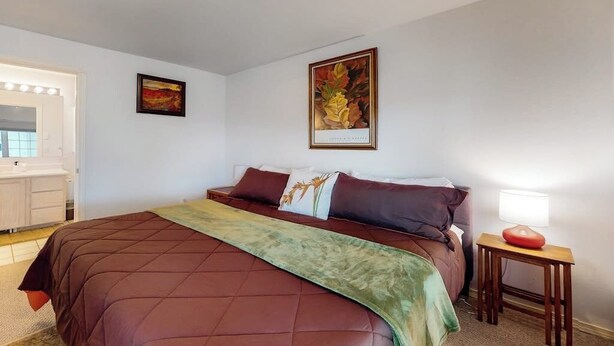 Een slaapkamer met een bed, een nachtkastje met een lamp, een spiegel en twee ingelijste foto's aan de muur.