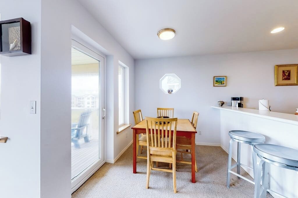 Un espace repas comprenant une table et des chaises, un comptoir de bar avec des tabourets et une fenêtre donnant sur un paysage agréable.
