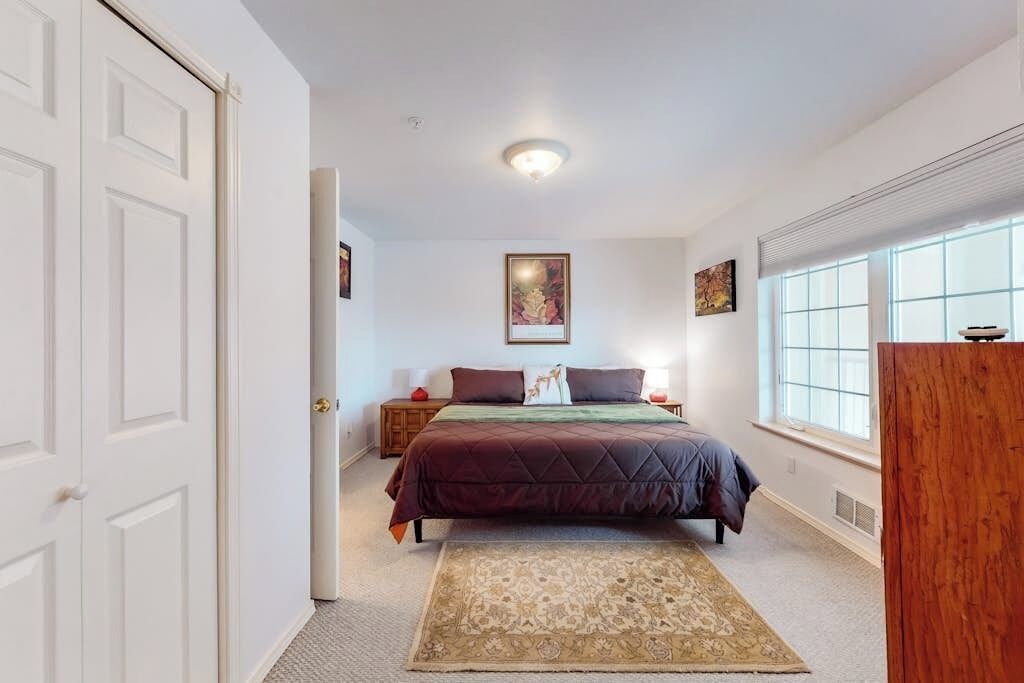 Un dormitorio con cama, mesita de noche, ventana y puerta.