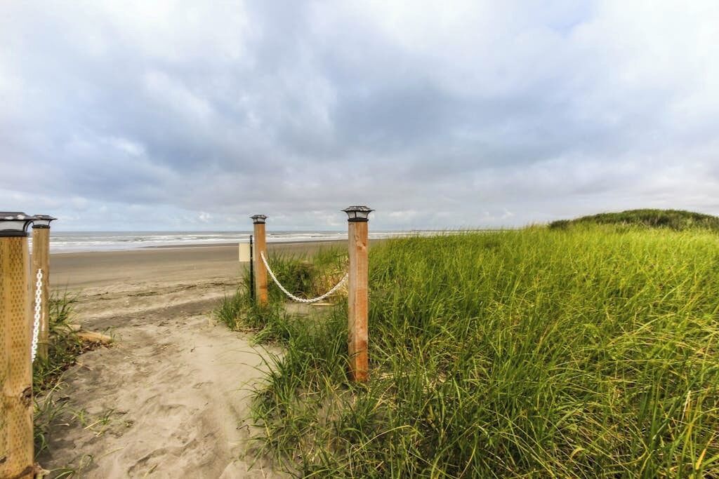 A pathway leading to a beach with a chain barrier and lamp posts.
