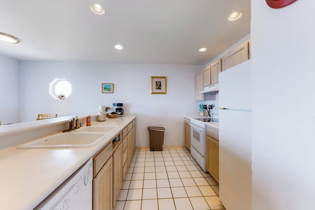 A compact kitchen with a dishwasher, a sink, and a trash bin.