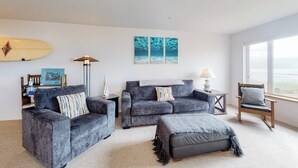 Een woonkamer met een bank, poef en fauteuil, een surfplank en kunst aan de muur.