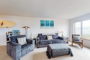 Een woonkamer met een bank, poef en fauteuil, een surfplank en kunst aan de muur.