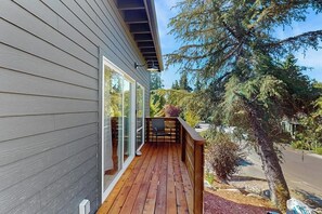 A wooden deck with a chair and a glass door leading to a room. - 1BR Home great for work, play, easy Seattle access (Bainbridge Island)