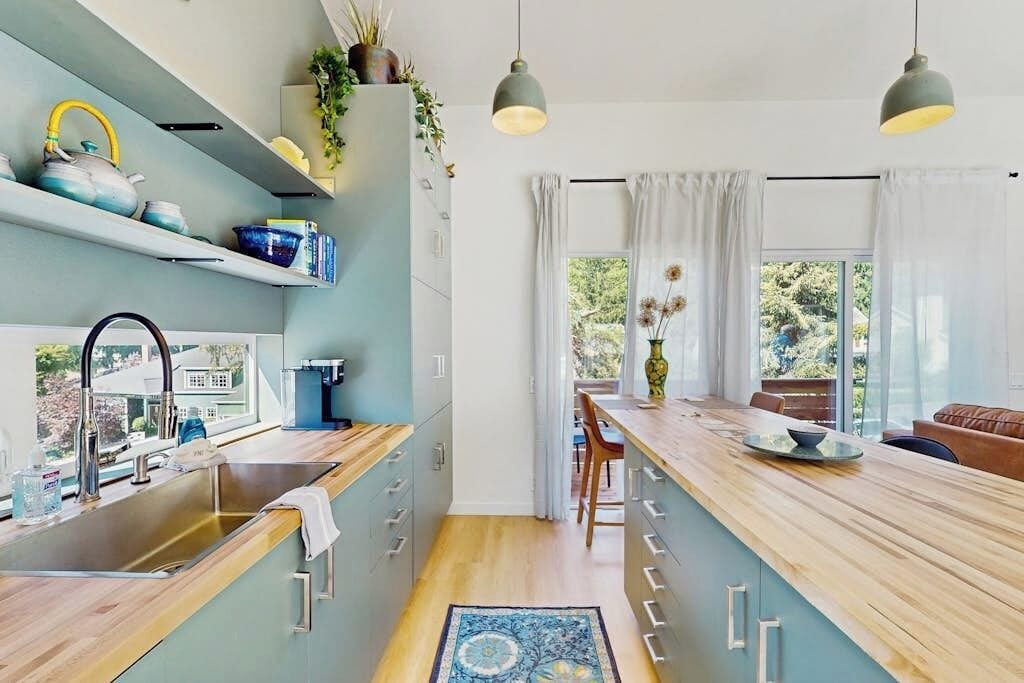 A modern kitchen with a wooden countertop, stainless steel sink, and pendant lighting.