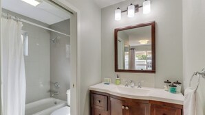 A bathroom with a bathtub, toilet, vanity with drawers, and a mirror. - Downtown | Lakeview | Deck | Hot Tub (Mercer Island)
