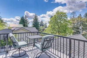 Un balcon avec une table et deux chaises, donnant sur un quartier résidentiel bordé d’arbres et de maisons.
