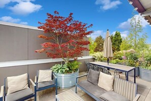 Ein Sitzbereich im Freien mit Tisch und Stühlen, einem Blumentopf und einem Baum mit roten Blättern.