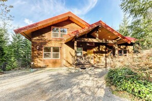 A wooden cabin with a sloped roof, a porch, and a gravel driveway surrounded by trees. - 4BR Mountainview Dog Friendly - Hot Tub - Deck (Skykomish)