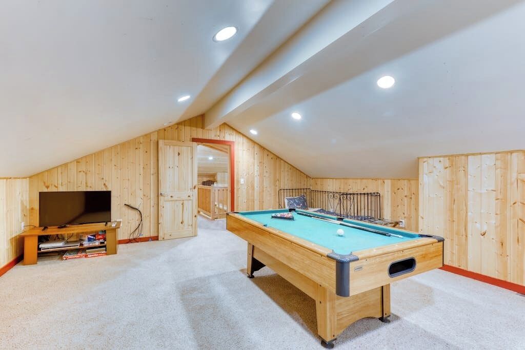 Une pièce avec une table de billard, un téléviseur et un plafond en bois.