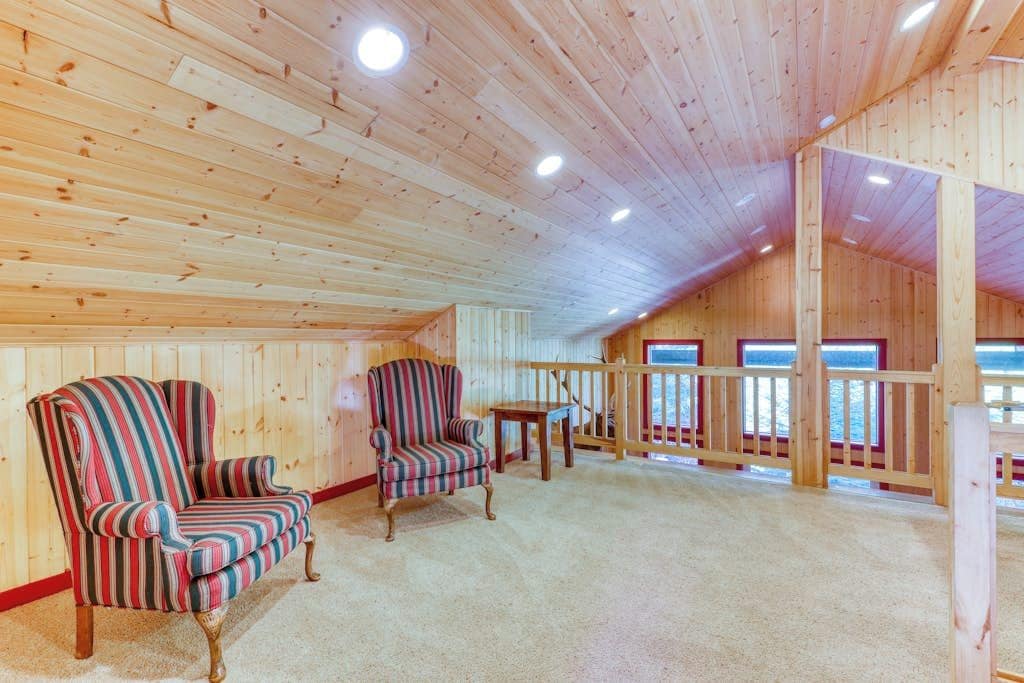 Ein geräumiger Raum mit Holzwänden und -decken, ausgestattet mit zwei gestreiften Sesseln und einem kleinen Tisch.