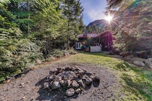 Eine Holzhütte, umgeben von dichtem Wald, mit einem Feuerkorb im Vordergrund.
