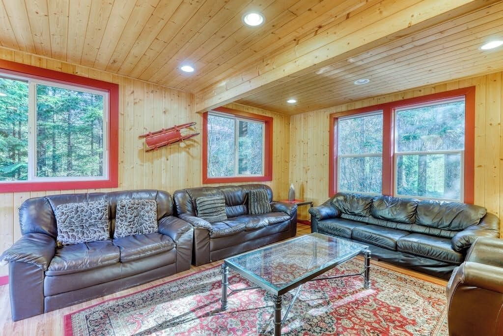 Una habitación con paneles de madera, dos sofás de cuero, una mesa de centro de vidrio y una alfombra roja estampada.