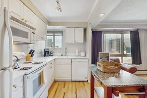 A compact kitchen with white appliances, a dining area with a granite countertop, and a view of the city through a large window. - Downtown 1BR Washington State Conv. Center 14th-fl (Seattle)