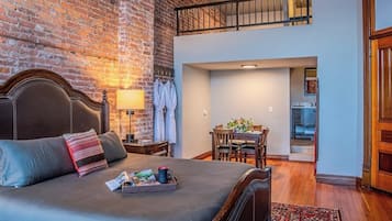 A bedroom with a large bed, a wooden headboard, a nightstand, a lamp, and a brick wall.