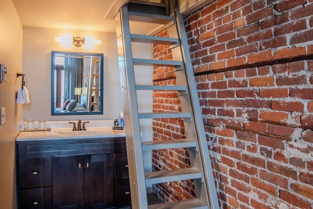 A bathroom with a dark wooden vanity, a mirror, and a brick wall.