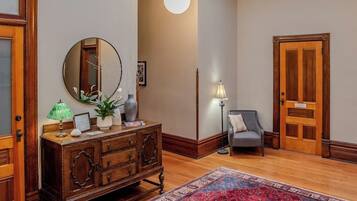 A room with a wooden dresser, a round mirror, a lamp, a chair, and a patterned rug.