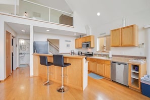 A modern kitchen with a central island, bar stools, wooden cabinets, a dishwasher, and a microwave.