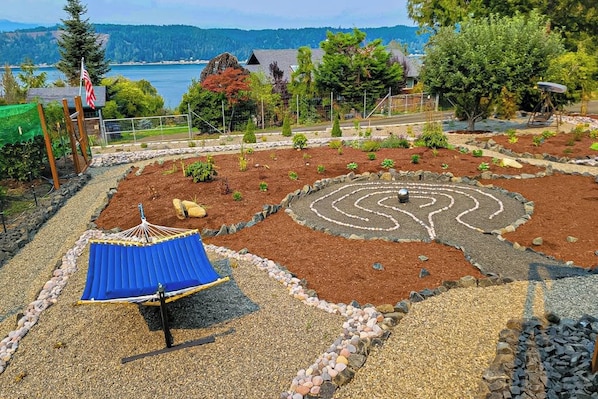A garden with a circular maze, a hammock, and a view of a lake.