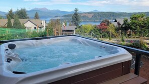 A hot tub with a wooden deck and a view of a lake and mountains.