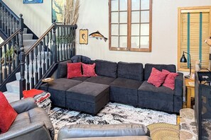 Ein Wohnzimmer mit einem Ecksofa, einer Treppe und einem großen Fenster.