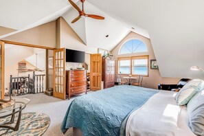 Ein Schlafzimmer mit einem großen Bett, einem Deckenventilator, einem Schreibtisch und Meerblick durch ein Fenster.