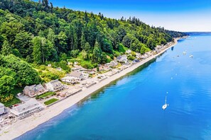 Eine Luftaufnahme einer Küstenstadt mit einem langen Strand, dicht bewaldeten Hügeln und klarem, blauem Wasser.