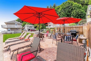 Ein Außenbereich mit einer Terrassenanlage, Lounge-Möbeln, einem Grill und roten Sonnenschirmen.