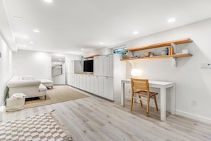 A modern kitchen with white cabinets, a dining area with a white table and chair, and a built-in TV. - Modern Studio - 1st Floor - 1 Block to Kerry Park (Seattle)