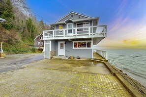 A two-story waterfront property with a balcony, a garage, and a paved driveway leading to the water.