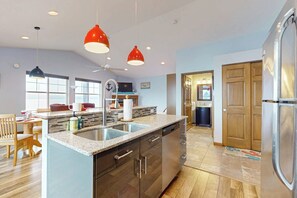 A modern kitchen with granite countertops, stainless steel appliances, and red pendant lighting.
