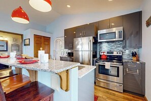 A modern kitchen with stainless steel appliances, a granite countertop, and wooden accents.