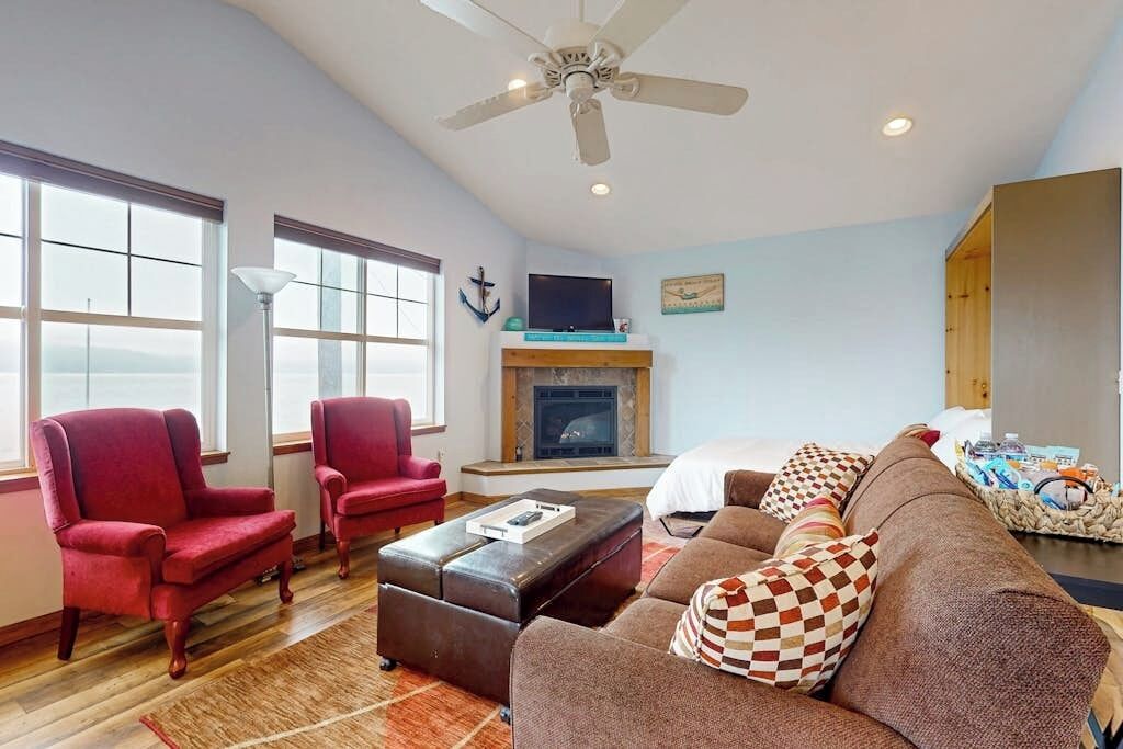 A spacious living room with a fireplace, a ceiling fan, and a large window providing a view of the outdoors.