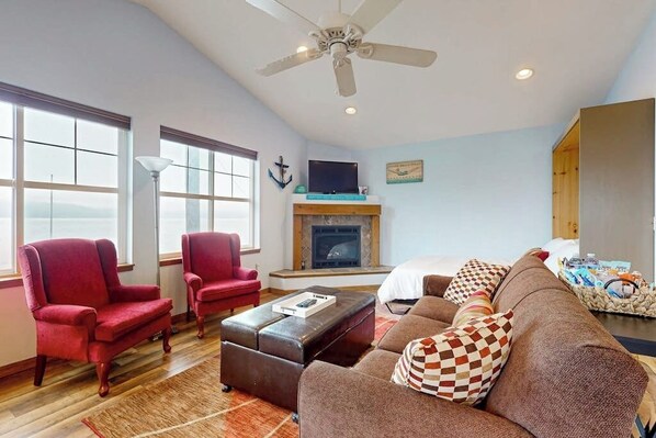 A spacious living room with a fireplace, a ceiling fan, and a large window providing a view of the outdoors.