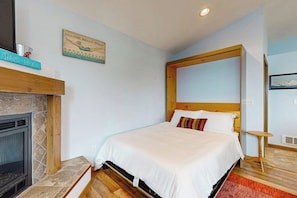 A bedroom with a bed, a fireplace, and a wall-mounted picture.