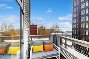 Ein Balkon mit einer Couch und Kissen mit Blick auf eine Stadtlandschaft.