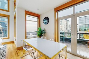 Ein modernes Interieur mit einem weißen Tisch, klaren Stühlen, einer Zimmerpflanze und einem großen Fenster mit Blick auf Gebäude.