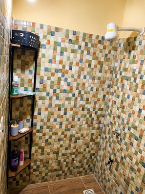 Un espacio de ducha con pared de azulejos, repisa con artículos de aseo y cabezal de ducha.