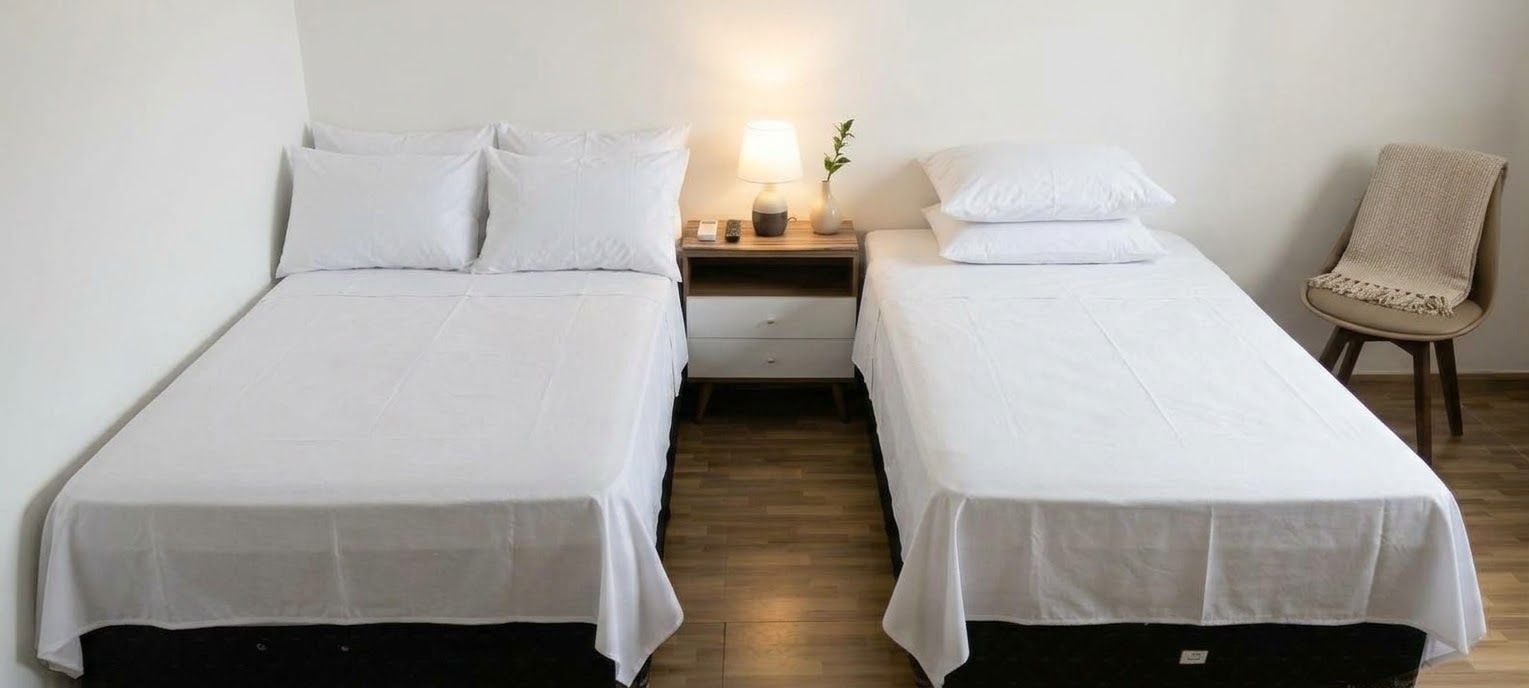 Een kamer met twee eenpersoonsbedden, een nachtkastje met lamp, een stoel en een houten vloer.
