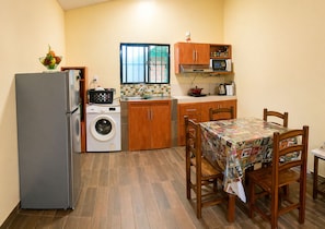 A compact kitchen with a refrigerator, washing machine, microwave, and wooden cabinets.