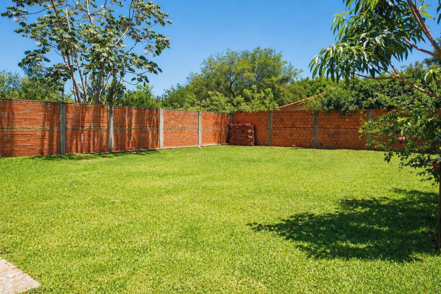 Un patio trasero bien cuidado con un muro de ladrillo, césped y árboles.