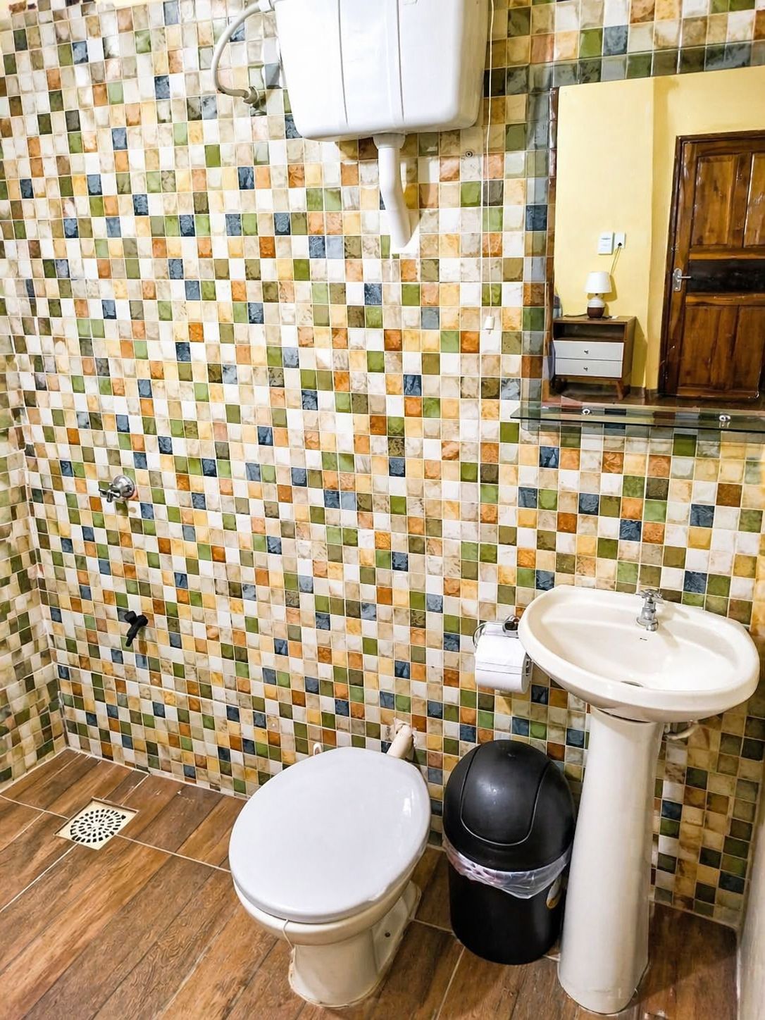 Kylpyhuone, jossa on laatoitettu mosaiikkiseinä, valkoinen pesuallas ja wc-istuin.