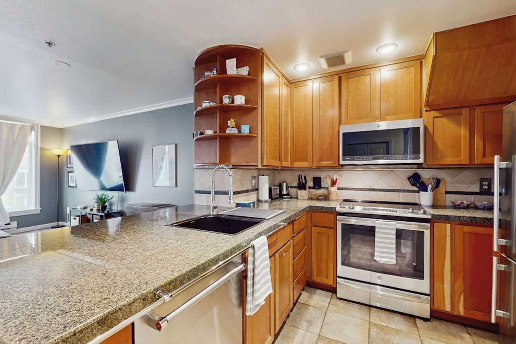 A modern kitchen with granite countertops, wooden cabinets, stainless steel appliances, and a built-in microwave.