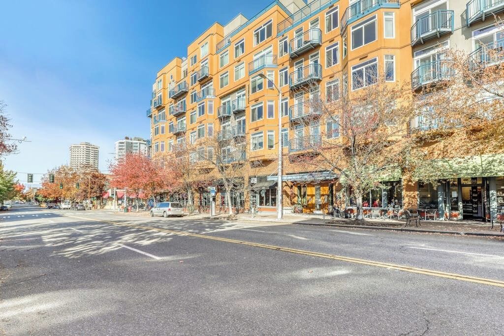A multi-story residential building with balconies, a crosswalk, and autumn trees.