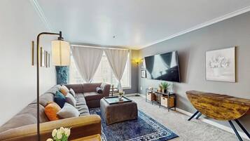 A modern living room with a sofa, ottoman, coffee table, TV, and a wooden side table.