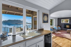 A modern kitchen with a large window overlooking a lake, a fireplace, and a cozy seating area. - 3BR waterfront home, private hot tub and game room (Gig Harbor)