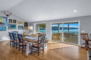 A dining area with a wooden table and chairs, a large window with a view of the water, and artwork on the walls. - 3BR waterfront home, private hot tub and game room (Gig Harbor)
